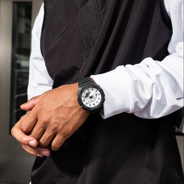 Person wearing a black watch with a white face, dressed in a white shirt and black vest.