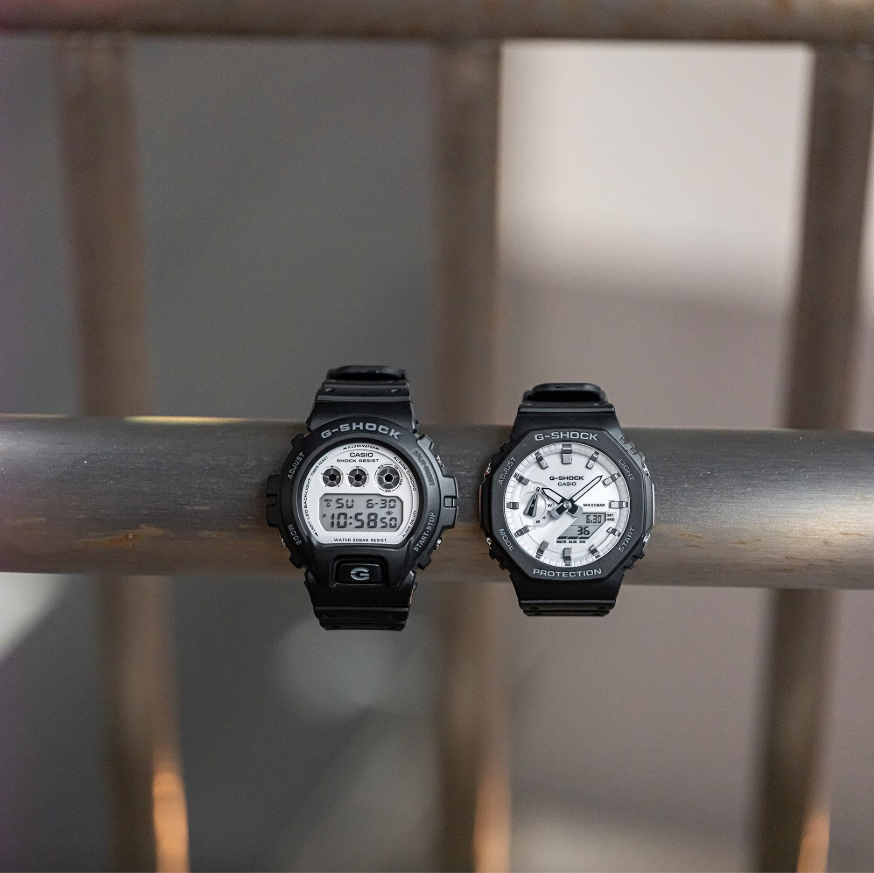 Two Casio G-Shock watches on a metal surface with a blurred background
