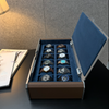 A luxury watch display box with an open lid, showcasing 12 different wristwatches arranged neatly inside. The box features a textured brown exterior, a deep blue velvet interior, and silver-tone metal hinges.