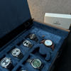 Close-up of the AUBLIQ watch box interior with blue watch cushions, one empty watch slot and a covered strap compartment.