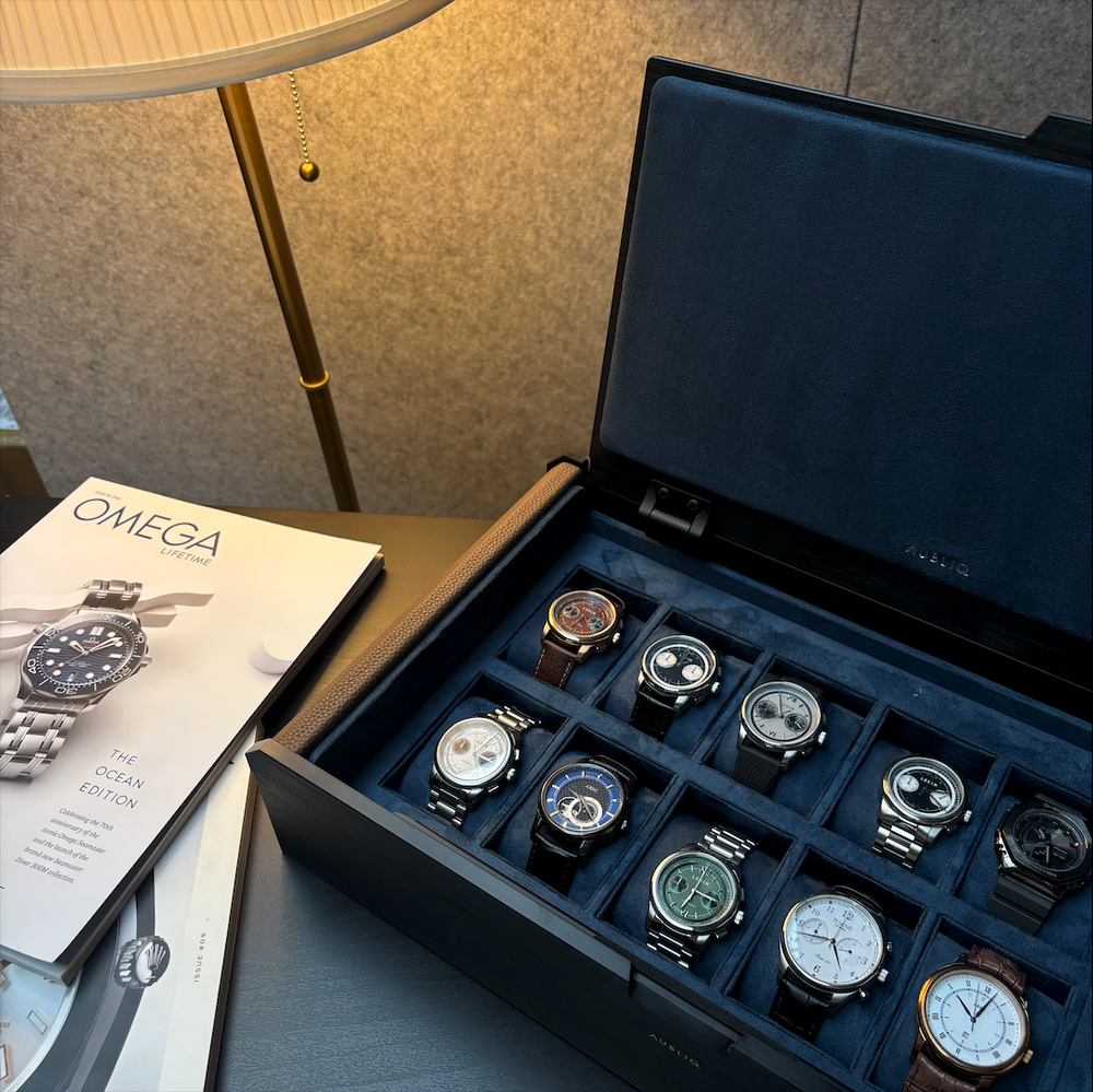 AUBLIQ black and brown watch box displaying ten watches in individual blue-lined compartments beneath an open padded lid.