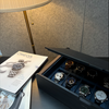 AUBLIQ black and brown watch box with lid partly open, displaying watches in blue-lined slots beside watch magazines.